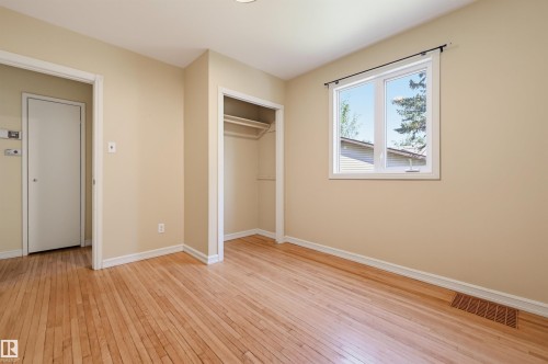 Room featuring wood-finish flooring, a double-hung window, white trim throughout, an open closet with a hanging rod, and a solid white door - 7754 80 Avenue Nw, Edmonton, AB - Indoor Photo Showing Other Room