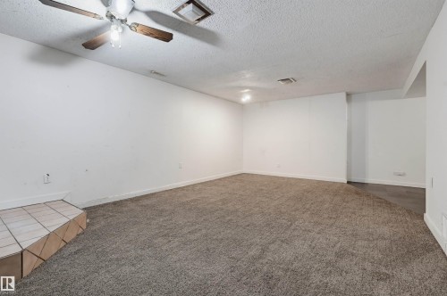 Expansive carpeted room featuring a ceiling fan with light fixture, recessed lighting, and a ceramic tile-finished architectural element - 7754 80 Avenue Nw, Edmonton, AB - Indoor Photo Showing Other Room