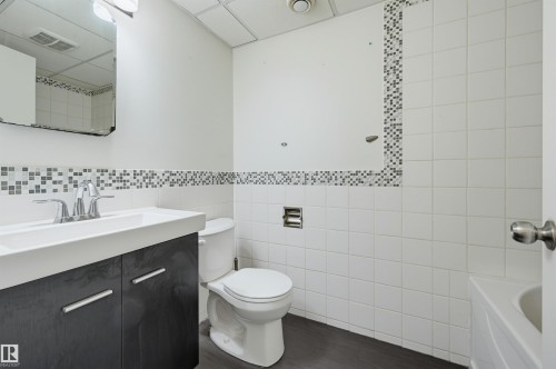 Bathroom featuring a dark wood-finish vanity with an integrated white sink, chrome faucet, and a wall-mounted mirror - 7754 80 Avenue Nw, Edmonton, AB - Indoor Photo Showing Bathroom