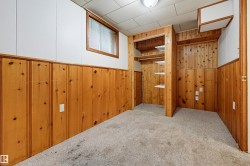 Carpeted room featuring wood-finish paneling, white upper walls, a built-in closet with shelving, and a window with wood trim - 
