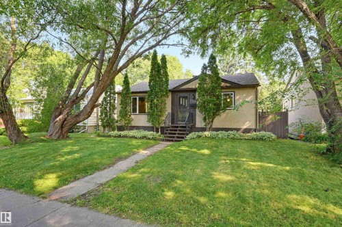 Exterior stucco facade with a dark trim, complemented by established trees and a manicured lawn - 7754 80 Avenue Nw, Edmonton, AB - Outdoor