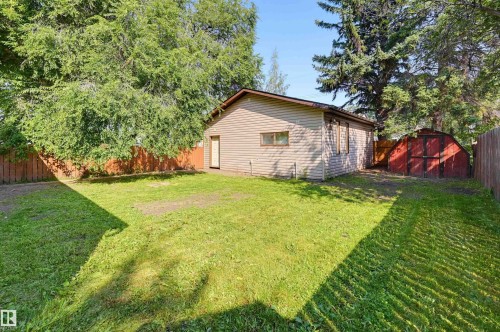 Spacious backyard featuring a detached accessory building with siding, a separate red storage shed, mature perimeter trees, and a full privacy fence - 7754 80 Avenue Nw, Edmonton, AB - Outdoor