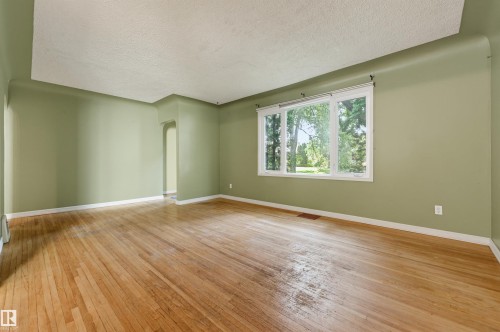 Expansive room featuring light wood-finish flooring, a large multi-pane window with white trim, and a textured ceiling - 7754 80 Avenue Nw, Edmonton, AB - Indoor Photo Showing Other Room