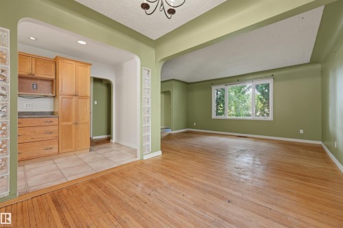 Hardwood flooring extends across the primary space, complemented by a large window with natural light - 7754 80 Avenue Nw, Edmonton, AB - Indoor