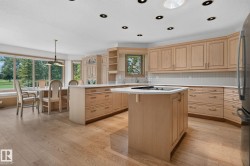 Open-concept kitchen and dining area featuring light wood-finish cabinetry, a central island with a built-in cooktop, and light wood-finish flooring - 