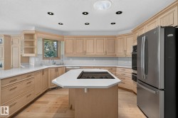 Kitchen featuring natural wood cabinetry, white countertops, a built-in cooktop island, stainless steel appliances, and recessed lighting - 