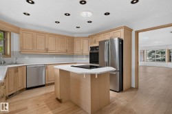 Kitchen with light wood cabinetry, a central island featuring a black cooktop, and a stainless steel appliance suite including a refrigerator, dishwasher, and built-in oven - 