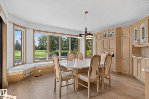 Dining area featuring a curved bay window with a built-in window seat, wood-finish flooring, and a comprehensive built-in cabinetry system with decorative glass accents - 120 Ironwood Place Nw, Edmonton, AB - Indoor Photo Showing Dining Room