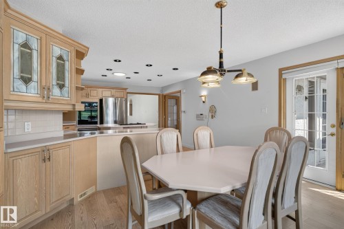 Dining area with light-toned wood-finish flooring, a multi-light chandelier, and double glass-paneled doors - 120 Ironwood Place Nw, Edmonton, AB - Indoor Photo Showing Dining Room