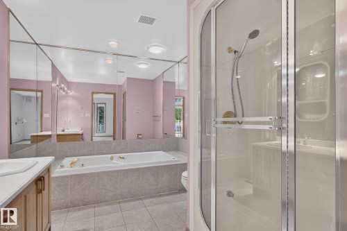 Bathroom featuring a built-in tub with tile surround, glass-enclosed shower, wood-finish vanity with countertop, and expansive wall-mounted mirror - 120 Ironwood Place Nw, Edmonton, AB - Indoor Photo Showing Bathroom
