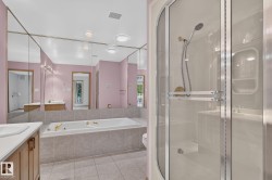Bathroom featuring a built-in tub with tile surround, glass-enclosed shower, wood-finish vanity with countertop, and expansive wall-mounted mirror - 