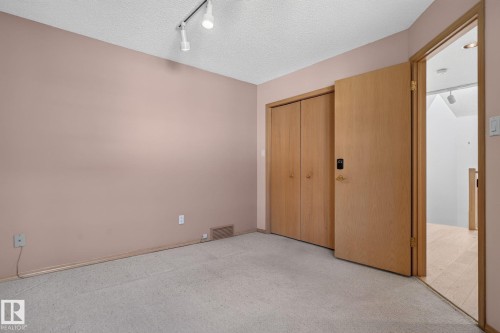 Carpeted room with track lighting, beige walls, and wood-finish bifold closet doors - 120 Ironwood Place Nw, Edmonton, AB - Indoor Photo Showing Other Room