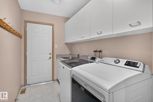 Functional laundry area featuring white upper cabinetry, a utility sink, and tiled flooring - 120 Ironwood Place Nw, Edmonton, AB - Indoor Photo Showing Laundry Room