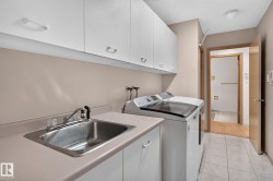 Utility room featuring white cabinetry, a stainless steel sink, light-toned countertops, and tile flooring - 