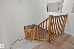 Stairwell with light wood banister and balusters, carpeted treads, and wood-finish flooring - 
