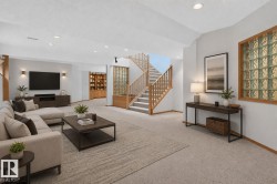 Spacious lower-level living area featuring recessed lighting, light-toned carpeting, and a wood-finish staircase with natural wood railings - 