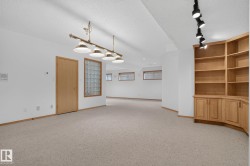Spacious room with light-colored carpeting, recessed lighting, and a multi-light pendant fixture - 