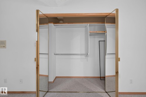 Mirrored bi-fold closet doors with brass-tone framing open to reveal an organized interior with multiple hanging rods and a shelf - 120 Ironwood Place Nw, Edmonton, AB - Indoor Photo Showing Other Room
