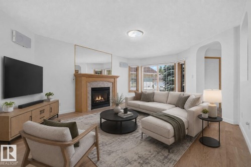Bright living area featuring a fireplace with a wood mantle and stone surround, wood-finish flooring, and arched entryway - 120 Ironwood Place Nw, Edmonton, AB - Indoor Photo Showing Living Room With Fireplace