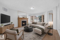 Bright living area featuring a fireplace with a wood mantle and stone surround, wood-finish flooring, and arched entryway - 