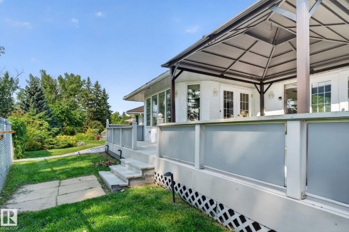 Expansive backyard featuring a covered patio, multiple windows, double French doors, a manicured lawn, and mature trees - 120 Ironwood Place Nw, Edmonton, AB - Outdoor