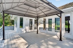 Expansive outdoor deck featuring a gazebo, white wood-finish flooring, and multiple glass-paned doors leading into the property - 