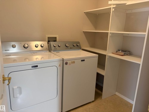 Laundry area with integrated white shelving units, a light-toned floor, and a neutral wall color - #209 8912 156 St Nw, Edmonton, AB - Indoor Photo Showing Laundry Room