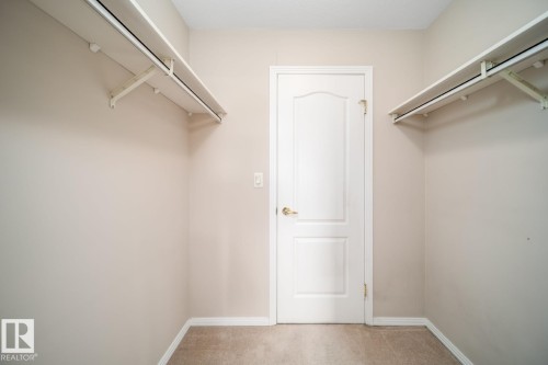 Carpeted flooring with built-in shelving, hanging rods, and a paneled door with brass hardware - #209 8912 156 St Nw, Edmonton, AB - Indoor With Storage