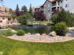 Community pond with fountain features, surrounded by lush green lawn, decorative rock beds, and mature landscaping - 