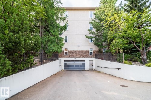 Multi-level building exterior featuring a stone and stucco finish, an integrated garage with a glass-paneled door, and a dedicated concrete entry ramp - #209 8912 156 St Nw, Edmonton, AB - Outdoor