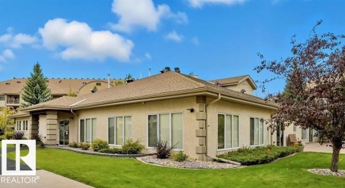 Stucco exterior with multiple windows, pitched shingle roof, manicured lawn, and planted garden beds - #209 8912 156 St Nw, Edmonton, AB - Outdoor