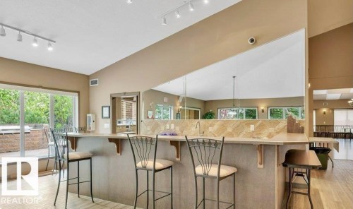 Breakfast bar with a stone-finish countertop, track lighting, a large window, and vaulted ceilings - #209 8912 156 St Nw, Edmonton, AB - Indoor Photo Showing Other Room