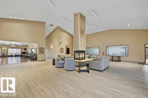 Spacious interior featuring vaulted ceilings, wood-finish flooring, a central fireplace, recessed lighting, and an open concept layout - #209 8912 156 St Nw, Edmonton, AB - Indoor