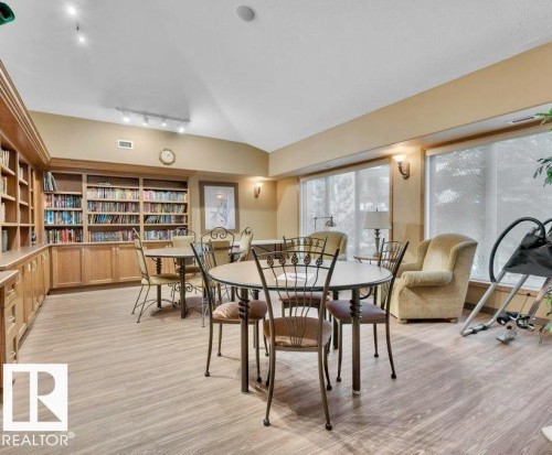 Built-in shelving and cabinetry, recessed ceiling lighting, wall sconces, large windows with roller blinds, and wood-finish flooring - #209 8912 156 St Nw, Edmonton, AB - Indoor Photo Showing Dining Room