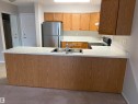 Kitchen featuring wood-finish cabinetry, stainless steel sink, light-toned countertops, and a full-size stainless steel refrigerator - #209 8912 156 St Nw, Edmonton, AB  - Indoor Photo Showing Kitchen With Double Sink 