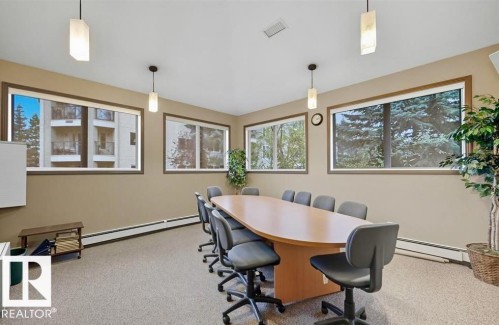 Carpeted room with multiple large windows, neutral-toned walls, and four pendant light fixtures - #209 8912 156 St Nw, Edmonton, AB - Indoor Photo Showing Office