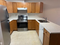 U-shaped kitchen featuring wood-finish cabinetry, stainless steel appliances, a double basin sink, and ample countertop space - 