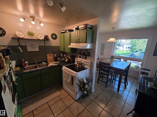 Kitchen featuring green cabinetry, a double basin stainless steel sink, black countertops, and a white electric range with overhead ventilation - 38 Greenwood Drive, Spruce Grove, AB - Indoor Photo Showing Other Room