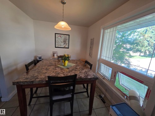 Dining area featuring an overhead pendant light with a fluted glass shade, tile flooring, a large window with multiple panes, and white walls - 38 Greenwood Drive, Spruce Grove, AB - Indoor Photo Showing Dining Room