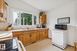 Kitchen featuring wood cabinetry with black hardware, a dual basin stainless steel sink, and a white tile backsplash - 