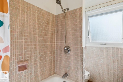 Bathroom featuring full wall square tile, a chrome shower fixture, and a white casement window - 12835 91 Street Nw, Edmonton, AB - Indoor Photo Showing Bathroom