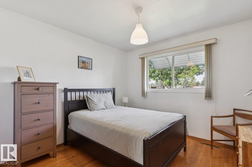 Bedroom featuring wood-finish flooring, a contemporary pendant light fixture, and a large window with horizontal blinds - 12835 91 Street Nw, Edmonton, AB - Indoor Photo Showing Bedroom