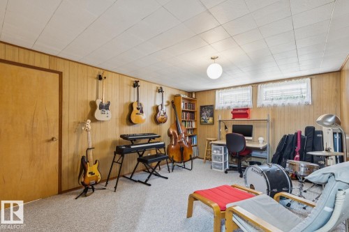 Carpeted room featuring wood-panel walls, a drop ceiling, and two upper-level windows - 12835 91 Street Nw, Edmonton, AB - Indoor Photo Showing Basement