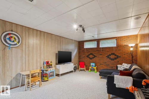 Carpeted room featuring wood-finish wall paneling and a brick accent wall with decorative patterning - 12835 91 Street Nw, Edmonton, AB - Indoor