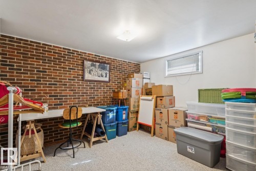 Lower-level room featuring an exposed brick accent wall, neutral carpeting, a ceiling-mounted light fixture, and a single window with blinds - 12835 91 Street Nw, Edmonton, AB - Indoor