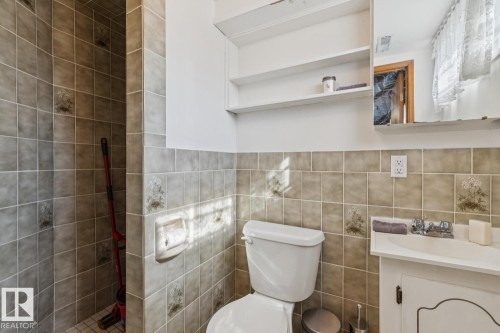Bathroom featuring full wall tiling, a built-in shower stall, a vanity with an integrated sink, a wall-mounted mirror, and open shelving - 12835 91 Street Nw, Edmonton, AB - Indoor Photo Showing Bathroom