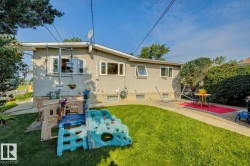 Expansive backyard featuring a manicured lawn, concrete patio areas, stucco exterior, and mature perimeter landscaping - 