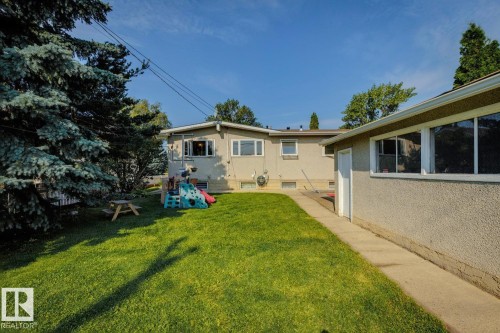 Expansive grass yard with mature evergreen trees, a concrete pathway, and stucco exterior finishes - 12835 91 Street Nw, Edmonton, AB - Outdoor
