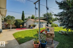 Spacious backyard featuring a concrete patio, expansive lawn, mature perimeter trees, a detached garage with stucco exterior, and a privacy fence - 