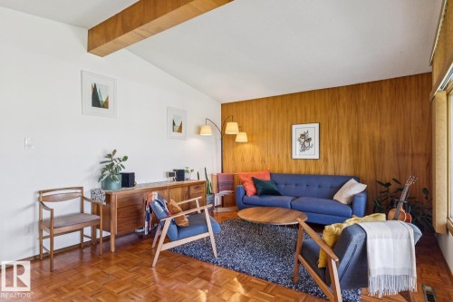 Living area featuring wood-finish flooring, a vaulted ceiling with exposed wood beam, and a wood-paneled accent wall - 12835 91 Street Nw, Edmonton, AB - Indoor Photo Showing Living Room